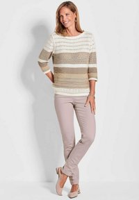 Maglione lavorato a maglia con strisce orizzontali in crema e beige, caratterizzato da dettagli a rete. Abbinato a pantaloni beige chiaro e ballerine color nude.