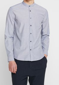 Långärmad skjorta med knappar i ljusblått tyg med ett subtilt strukturerat mönster. Har en bandkrage och svarta knappar. Matchande byxor visas inte.