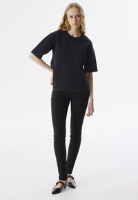 Camisa negra de manga corta con textura, combinada con pantalones negros ajustados y bailarinas negras, frente a un fondo neutro.