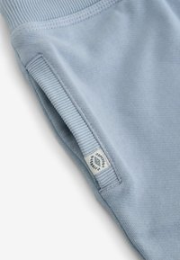Heledad sinised puuvillased üleülikonnad soonikuga kraega ning silt "Superdry Overalls" musta tekstiga. Sile tekstuur ja istuv disain.