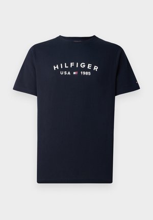 Marineblå bomull T-skjorte med kort erm. Har hvit trykt tekst: "HILFIGER USA 1985" og en liten logo på venstre erme.