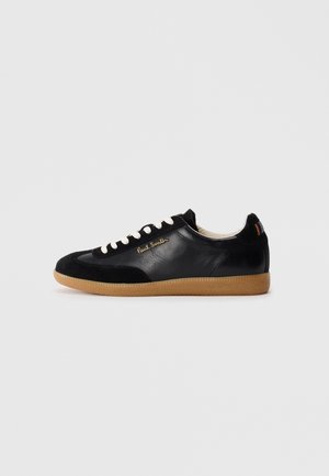 Black low-top leather sneaker with white laces, gum sole, "Paul Smith" gold logo on side, and multicolor striped detail on heel tab.
