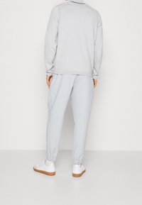 Ensemble de sport gris clair comprenant un haut zippé et un pantalon ajusté assorti. Texture lisse avec des poignets élastiques et des baskets blanches décontractées.
