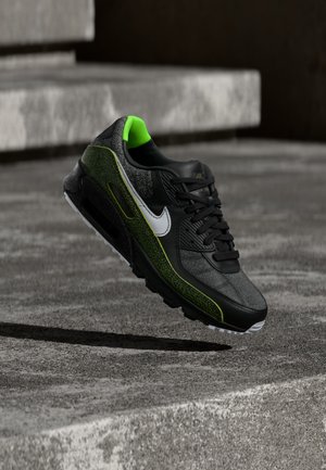 Sort og neongrøn Nike-sneaker med hvid swoosh, svævende over ru betontrapper i dæmpet belysning.