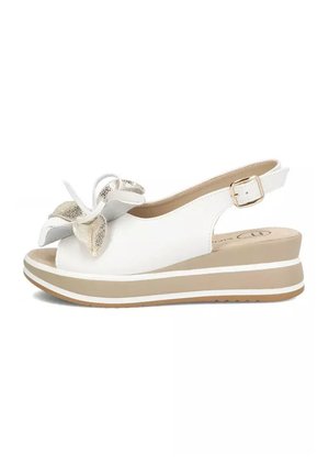 Biała sandałka na koturnie z beżową platformą, otwartym noskiem, paskiem na kostkę z klamrą i dekoracyjną dużą metalową kokardą z przodu.