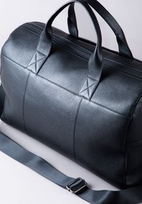 Black leather duffel bag with textured surface, dual handles, and an adjustable strap. Features horizontal stitching and a zippered closure.