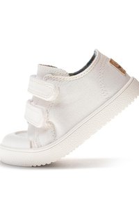 Zapatilla de lona blanca con dos correas de Velcro, punta redondeada y suela de goma texturizada. Presenta un pequeño detalle del logo en el lateral.
