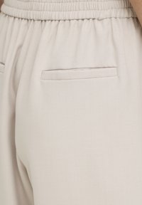 Close-up of light beige pants with elastic waistband and two horizontal back pockets on a person.