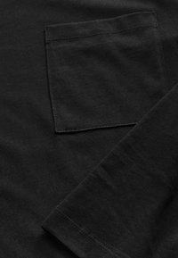 Fekete hosszú ujjú ing szövetének közelképe, amelyen négyzet alakú mellzseb és részletes varrás látható az ujj mandzsettáján.