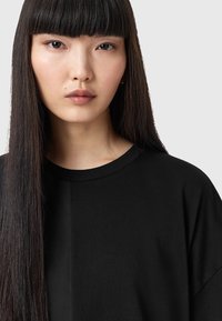 Sort oversized T-shirt med rund hals og korte ærmer, lavet af glat bomuldsstof. Har en let skinnende tekstur.