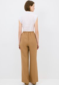 Witte mouwloze blouse met kraag, gecombineerd met lichtbruine, brede broek met een elastieken tailleband. Glad textuur van de stof.