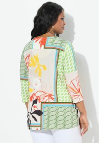 Bunt gemusterte Bluse mit Dreiviertelärmeln aus weichem Stoff. Sie weist abstrakte Muster und kontrastierende geometrische Akzente auf.