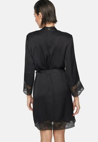 Robe en satin noir avec des manches trois-quarts bordées de dentelle et un ourlet, dotée d'une taille avec lien et d'un détail subtil au niveau de l'encolure arrière.