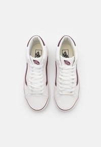 Baskets hautes blanches avec des accents bordeaux, cuir texturé, bout rond et lacets classiques. Présentent le logo Vans sur la languette et le côté.