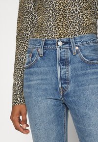 Topp med leopardmönster och långa ärmar, i kombination med högmidjade blå denimjeans med en urtvättad look, metallknapp och kontrasterande sömmar.