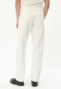 Pantalones de mezclilla blanca con un diseño de pierna recta, que cuentan con dos bolsillos traseros y una cinturilla minimalista. Acompañados de zapatos negros.