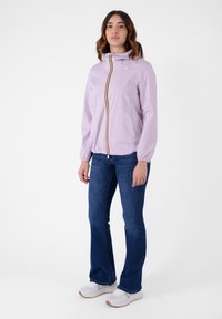 Giacca a vento zip-up di colore lilla con cappuccio, caratterizzata da una zip a strisce multicolori. Abbinata a jeans a zampa d'elefante blu e sneaker bianche.