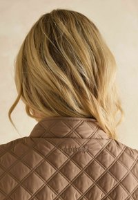 Braune gesteppte Jacke mit Rautenmuster und Stehkragen; verfügt über ein gesticktes "JOULES"-Logo auf dem Rücken. Glattes, leichtes Material.