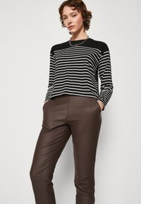 Haut rayé noir et blanc à manches longues associé à un pantalon en cuir synthétique marron. Le haut présente un col rond classique et une coupe décontractée.