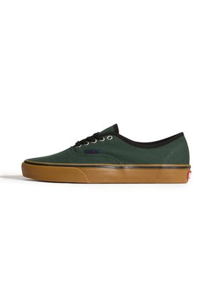 Zapatilla baja de lona verde oscuro con cordones negros, ribete negro, suela y puntera de goma marrón claro.