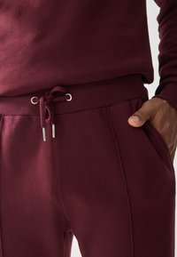Bordo trenirke z vrvico v pasu, kovinskimi oči in stranskimi žepi. Mehko bombažno blago z rebrastim pasom in manšetami.