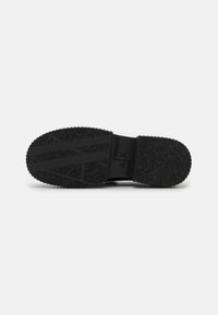 Suola di sneaker nera con motivo testurizzato per la presa, caratterizzata da un dettaglio logo in rilievo. Il materiale sembra gomma e il design è minimalista.