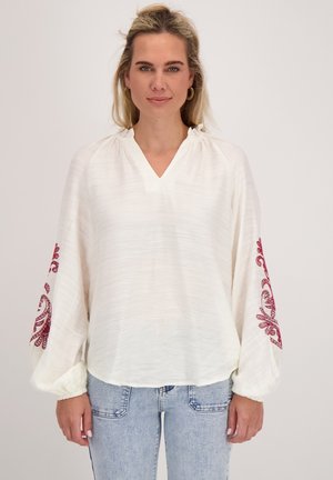 Witte blouse met V-hals, verstelbare halslijn en lange, wijdvallende mouwen met rode geborduurde patronen op elke mouw.
