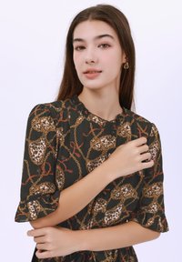 Černé šaty s leopardím potiskem a zlatým řetízkem, se ruflovým výstřihem a krátkými rukávy. Hladký materiál, detaily s knoflíky.
