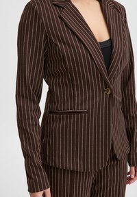 Blazer marrone a righe sottili con un solo bottone, revers a spillo e una tasca laterale. Il tessuto ha una consistenza liscia con righe bianche a contrasto.