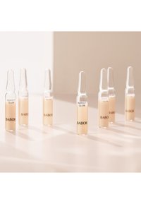 Sept ampoules en verre transparent contenant un liquide beige, étiquetées "PERFECT GLOW" et "BABOR", disposées sur une surface claire projetant des ombres douces.