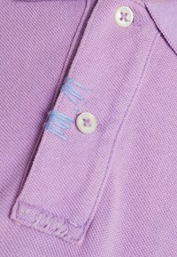 Světle fialová polo košile z látky s texturovaným tkaním, dvěma bílými knoflíky a malým modrým prošitím v blízkosti límce.