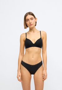 Zwarte beha met een diep decolleté en dunne bandjes, gecombineerd met zwarte slipjes met kant en een klein strikje in het midden.