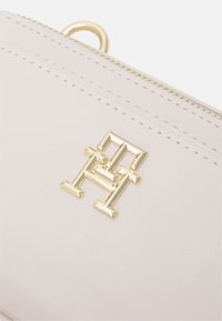 Monedero de cuero rosa claro con herrajes dorados, que presenta un diseño de logo elevado. Textura suave y costuras detalladas a lo largo de los bordes.