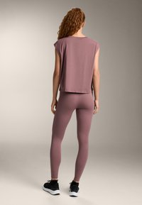 Top larg, cu mâneci scurte, de culoare mov liliachie, combinat cu colanți mulați asortați. Ținuta are o textură moale și un design simplu. Adidași negri.