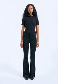 Black fitted t-shirt with a round neck, paired with high-waisted flared black jeans. Smooth texture, minimal detailing, and visible stitching.