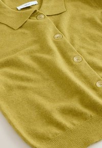 Haut en maille vert à manches courtes avec boutons, col et ourlet côtelé, posé à plat sur une surface blanche.