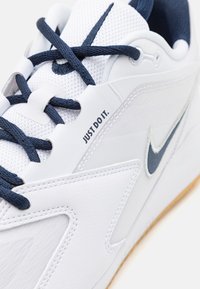 Witte sportieve schoen gemaakt van mesh en leer, met blauwe accenten, ronde veters en "JUST DO IT" gedrukt op de zijkant.