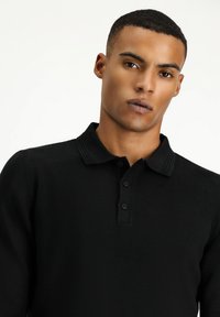 Schwarzes Strickpolohemd mit geripptem Kragen, drei-Knopf-Leiste und strukturierter Stoffoberfläche.