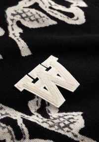 Crna pletena tkanina s kremastim uzorkom, s istaknutim teksturiranim bijelim logotipom "W". Dizajn kombinira kontrastne elemente i oblike.