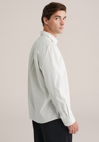 Balta medvilninė ilgomis rankovėmis marškiniai su klasikinėmis apykaklėmis, mygtukų rankovėmis ir laisvu kirpimu. Lygi tekstūra, paprastas dizainas be raštų.