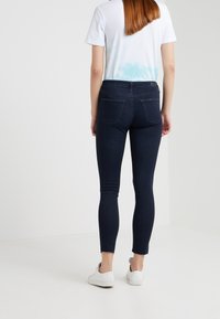 Mörkblå denim skinny jeans med en slät textur och medelhög midja. Har bakfickor och fransade fållar; bärs med en vit t-shirt och sneakers.