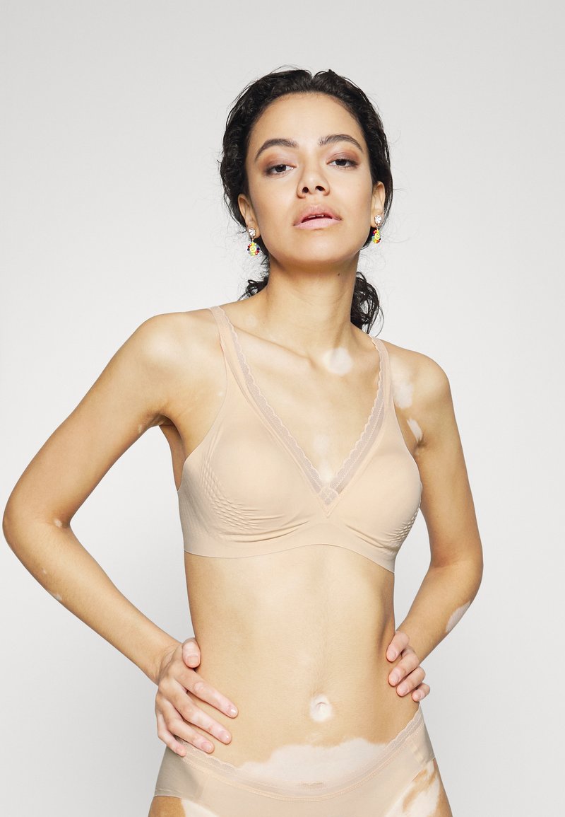 Soutien-gorge sans fil beige avec une texture douce, un design triangulaire et une finition en dentelle. Présente un motif ondulé et des bretelles ajustables.