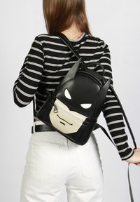 Mochila de imitación de cuero negra con diseño de Batman; cuenta con orejas puntiagudas, bolsillo blanco con cremallera para la cara y correas ajustables.
