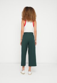 Groene wijde broek van zachte stof met een hoge taille en een gladde textuur. Gestyled met een wit tanktop en witte sneakers.