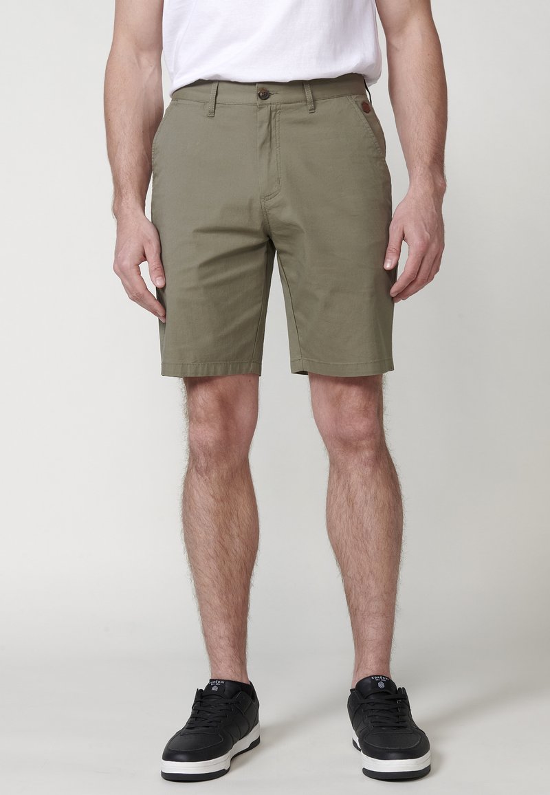 Olijfgroene shorts met een rechte snit, voorzien van een knoopsluiting, riemlussen en zijzakken. Draag het met zwarte schoenen.