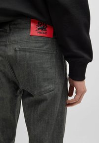 Harmaat farkut, joissa on sileä pinta. Takana punainen logopatch mustalla designilla, viisi-taskuinen tyyli ja kapea malli.