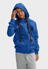 Blaue Zip-Hoodie mit gefütterter Kapuze, gerippten Bündchen und Logo-Detail auf der Brust, kombiniert mit grauen Sweatpants. Glatter Stofftextur.