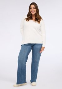 Cremefarbener Strickpullover mit langen Ärmeln, kombiniert mit hellblauen Schlagjeans und off-white Canvas-Sneakers. Schlicht, lässige Passform mit geripptem Material.