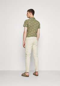 Kortærmet skjorte i gul med geometrisk mønster, kombineret med lyse beige bukser med opsmøg og brune sandaler.