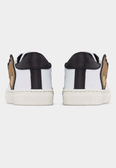 Ζευγάρι λευκά αθλητικά παπούτσια με μαύρες φτέρνες και σόλες, διακοσμημένα με μεγάλα καφέ πρόσωπα αρκουδάκια στη εξωτερική πλευρά.